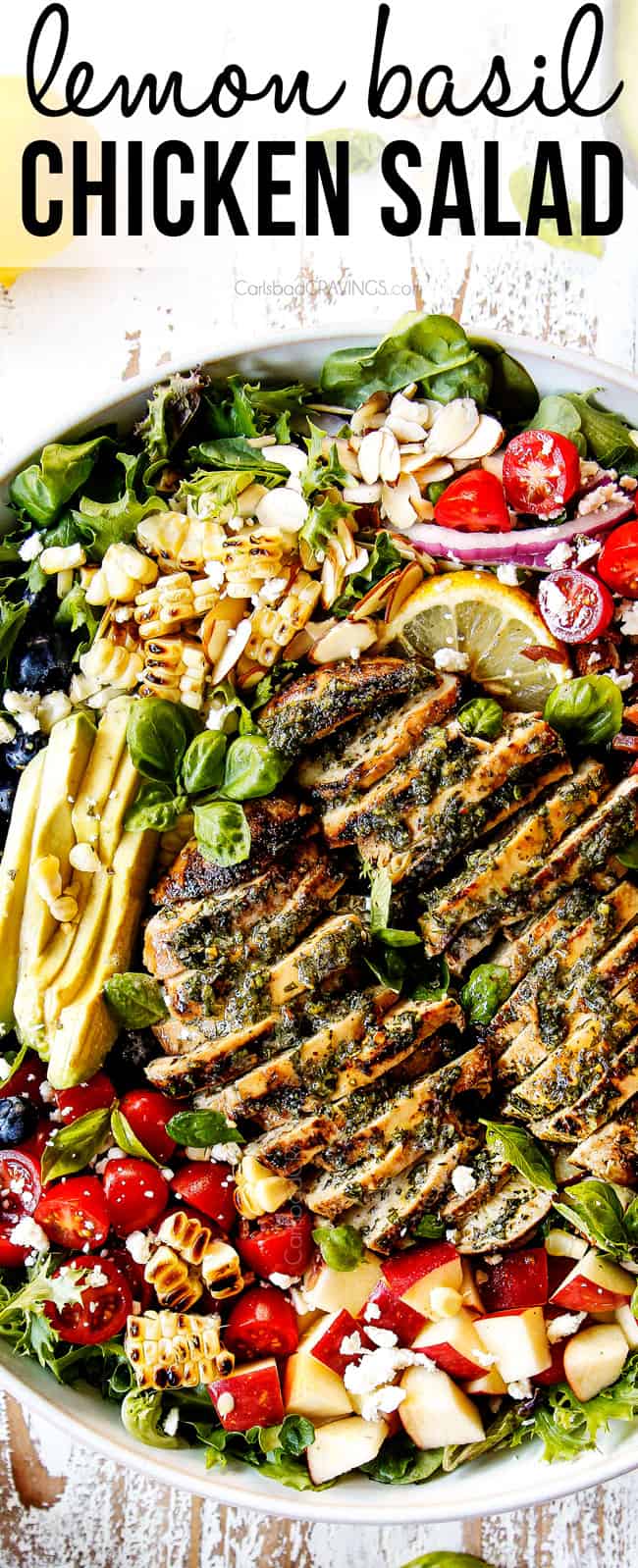 top view of grilled chicken salad in a white bowl with avocados, tomatoes, almonds, apples and blueberries