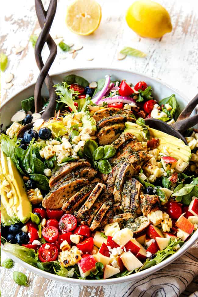 showing how to make grilled chicken salad recipe by tossing ingredients together in a white bowl with tongs.