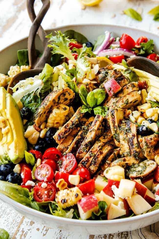 side view of showing how to make grilled chicken salad recipe by tossing grilled chicken, avocados and bacon together in a white bowl.