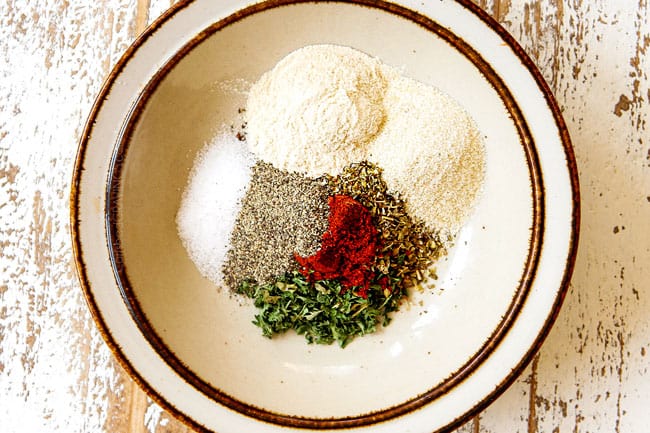 showing how to make Parmesan crusted chicken recipe by adding dried basil, dried parsley, dried oregano, salt, pepper and paprika to a bowl