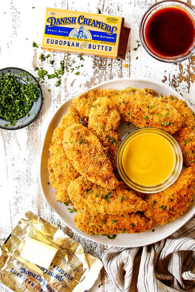 top view of baked Parmesan crusted chicken stacked on a white platter garnished with parsley