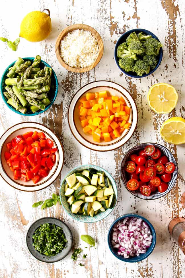 top view of pasta primavera recipe ingredients in bowls: broccoli, squash, zucchini, asparagus, bell peppers, tomatoes, peas, Parmesan, red onion, lemon juice and basil