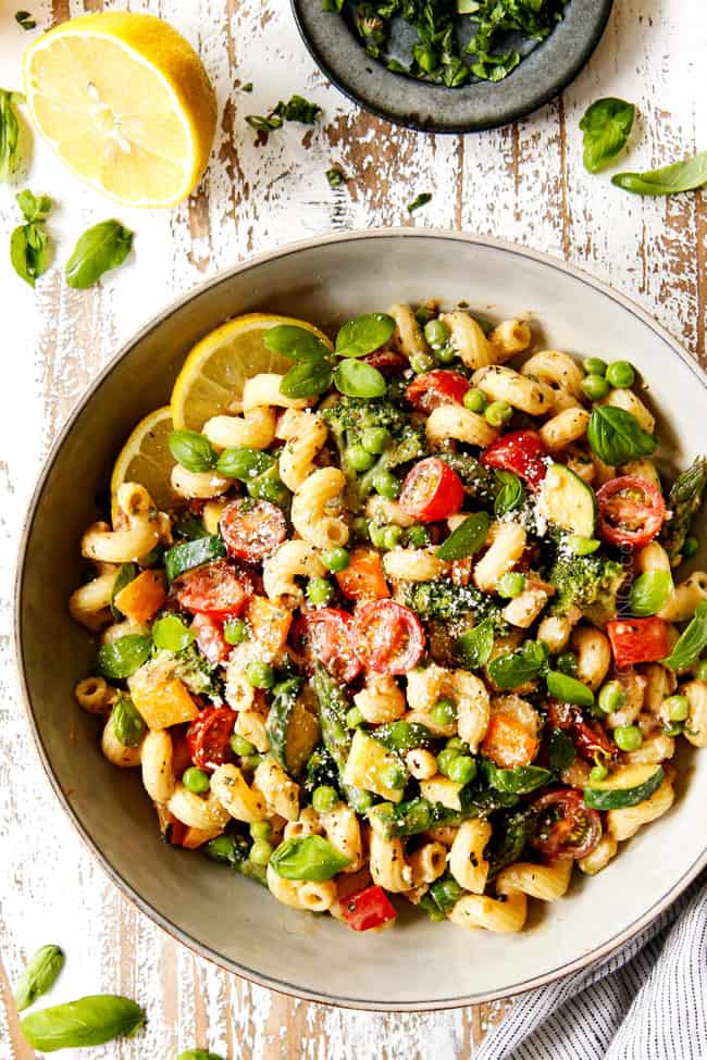 top view of creamy pasta primavera in a grey bowl garnished with Parmesan and fresh basil