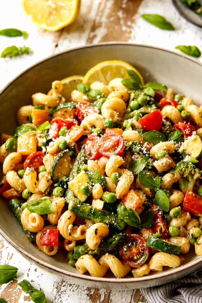 creamy pasta primavera in a grey bowl garnished with Parmesan and fresh basil