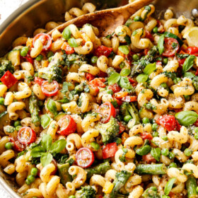 two hands holding pasta primavera recipe in a grey bowl garnished with Parmesan and fresh basil