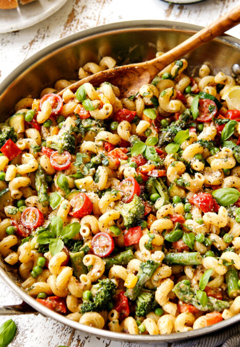 two hands holding pasta primavera recipe in a grey bowl garnished with Parmesan and fresh basil