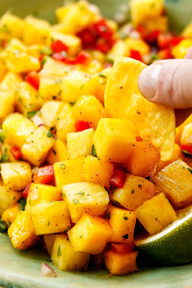 showing how to eat pineapple mango salsa by dipping a tortilla chip in the salsa