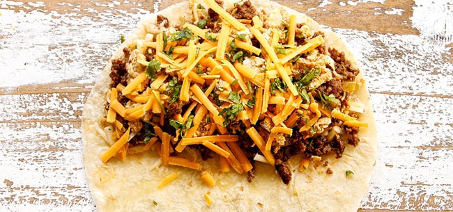 showing how to make breakfast quesadilla recipe by layering half of the tortilla with cheese, sausage, eggs and cilantro