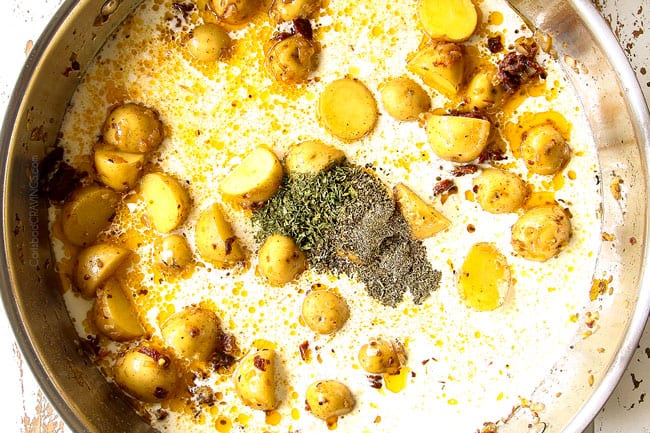 showing how to make creamy Tuscan chicken by adding heavy cream, chicken broth, garlic, sun-dried tomatoes to a stainless steel skillet