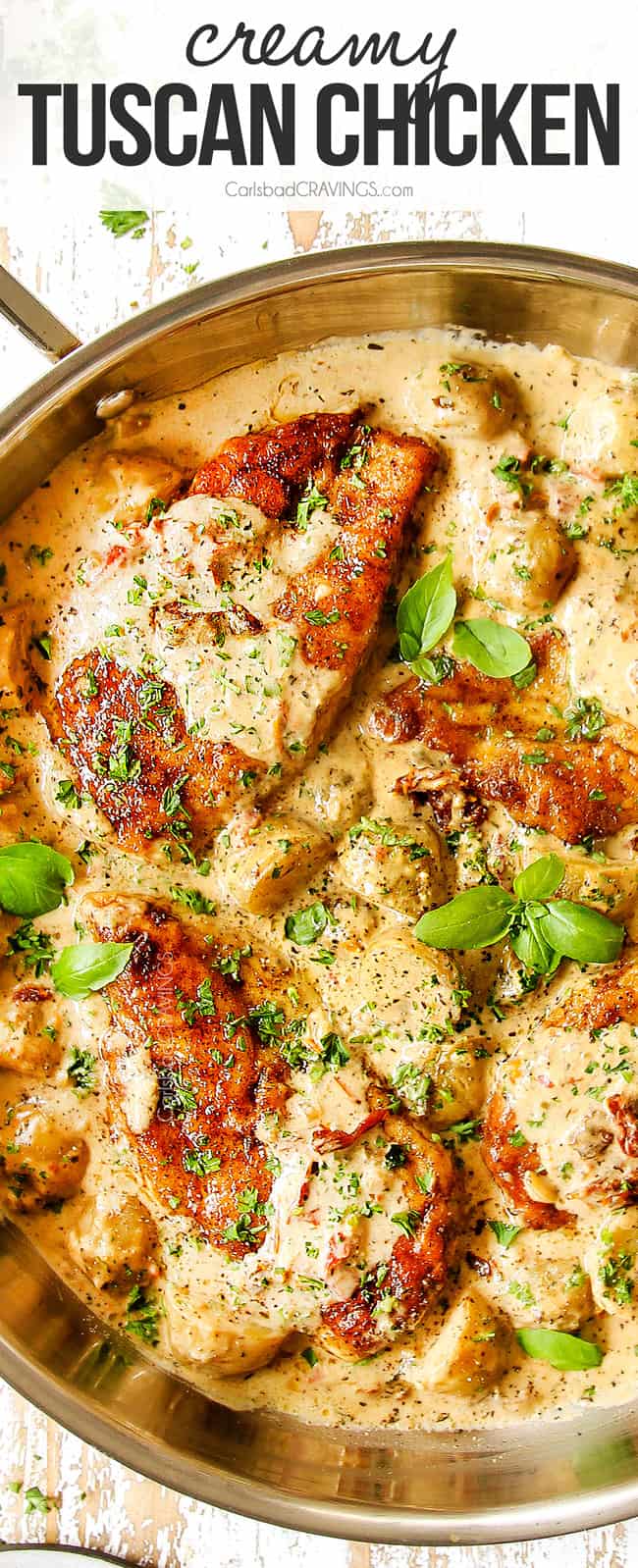 top view of creamy Tuscan chicken in a stainless steel skillet garnished b basil