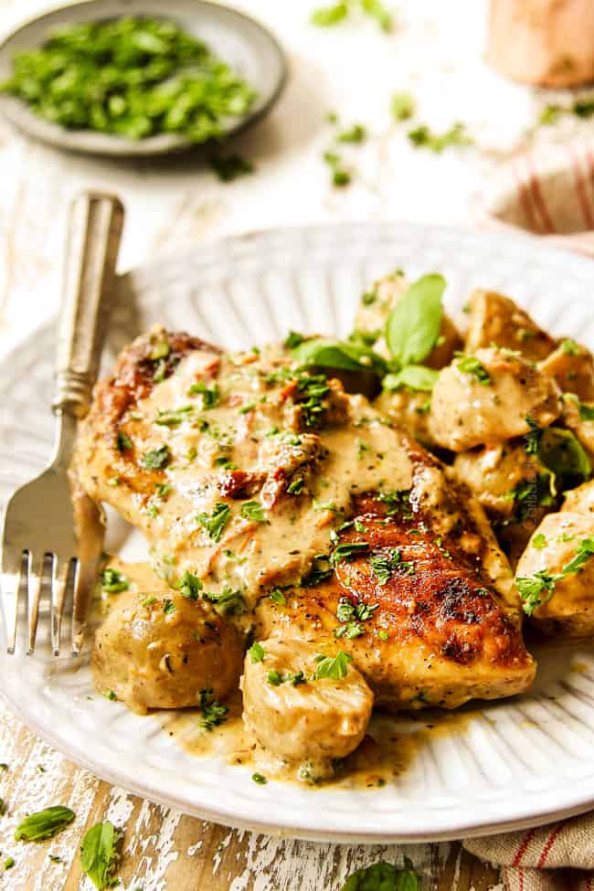 creamy Tuscan chicken breast on a white plate with garlic cream sauce and potatoes