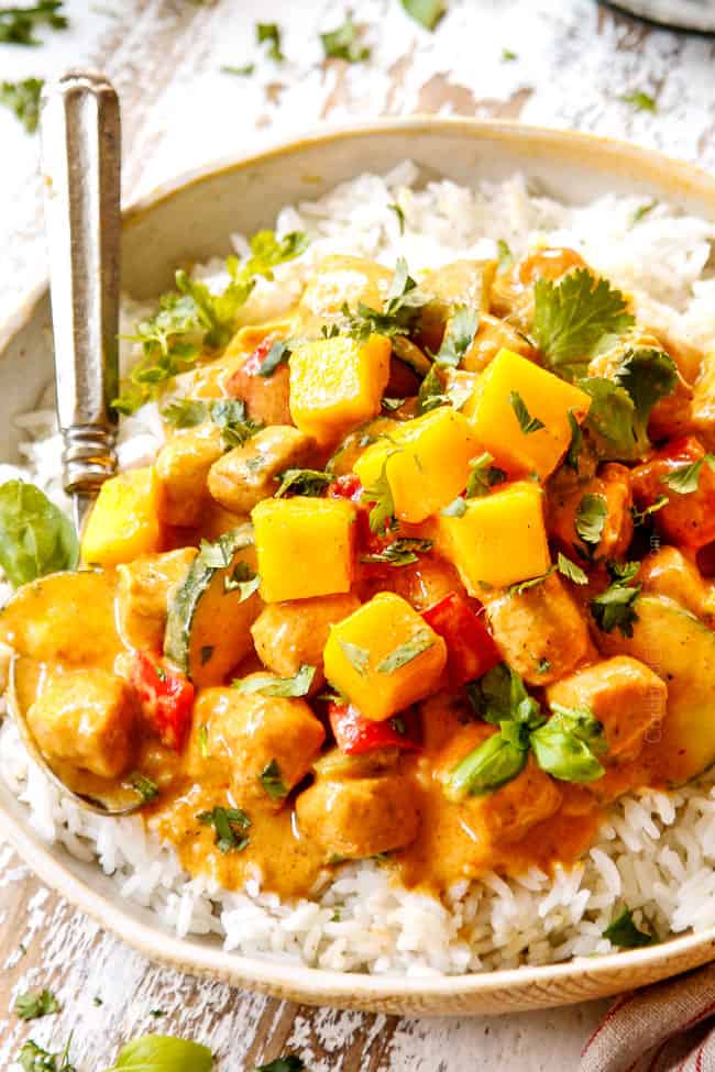 side view of mango chicken recipe with bell peppers in a tan bowl garnished with fresh basil and cilantro