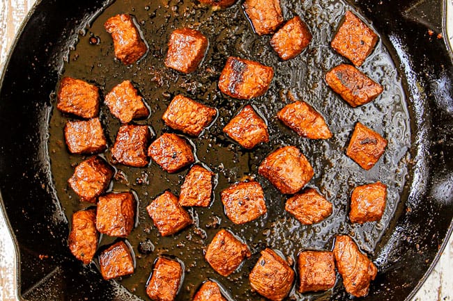 showing how to make steak and potatoes recipe by searing steak bites in a cast iron skillet