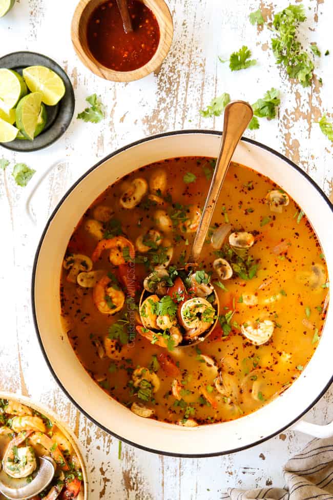 top view Thai Tom Yum Soup in a white soup pot with a ladle holding soup with shrimp