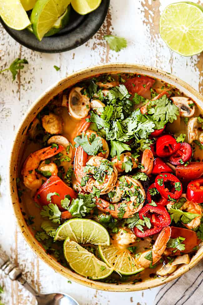 top view of a bowl of tom Yum Soup garnished with cilantro, lime and Thai red chilies