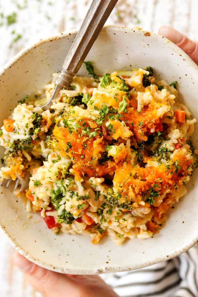 two hands holding a plate of chicken broccoli cheese rice casserole