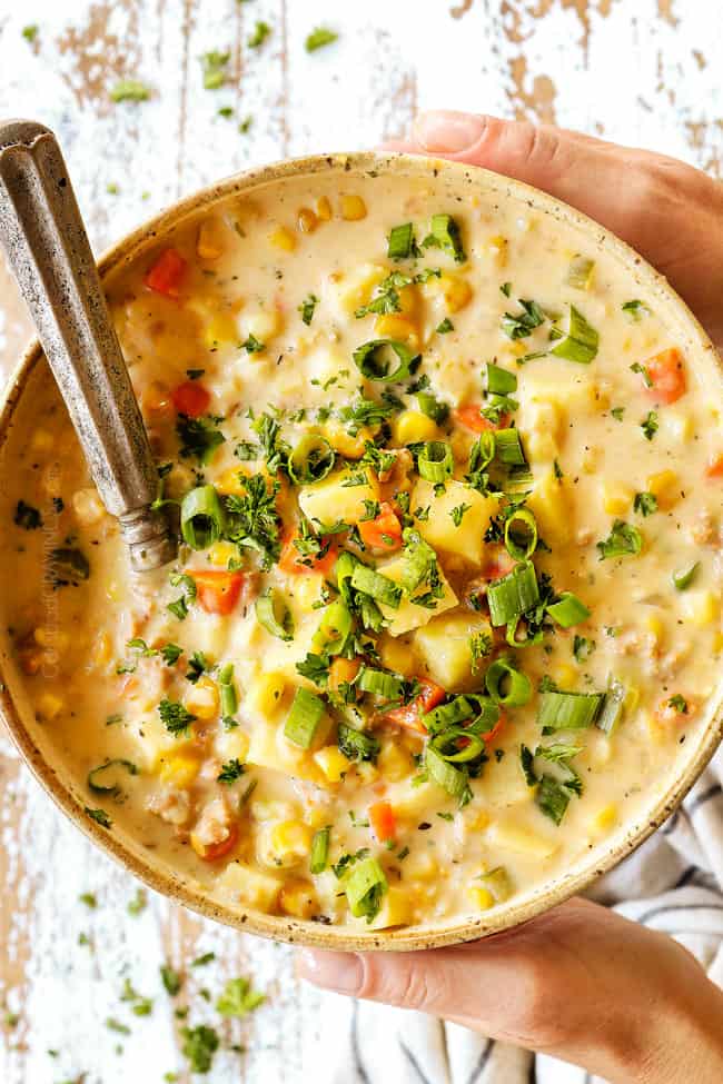 top view of two hands holding a bowl of corn chowder