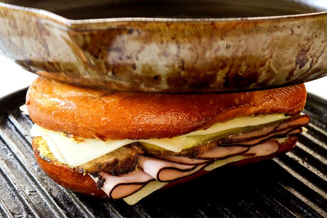 showing how to make Cuban sandwich recipe by toasting the Cubanos on a griddle pan and pressing down with a heavy skillet