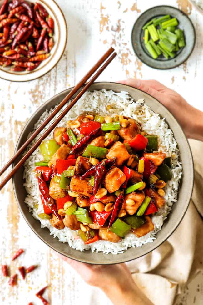 showing how to serve best kung pao chicken recipe by holding chicken in a bowl with rice and chopsticks