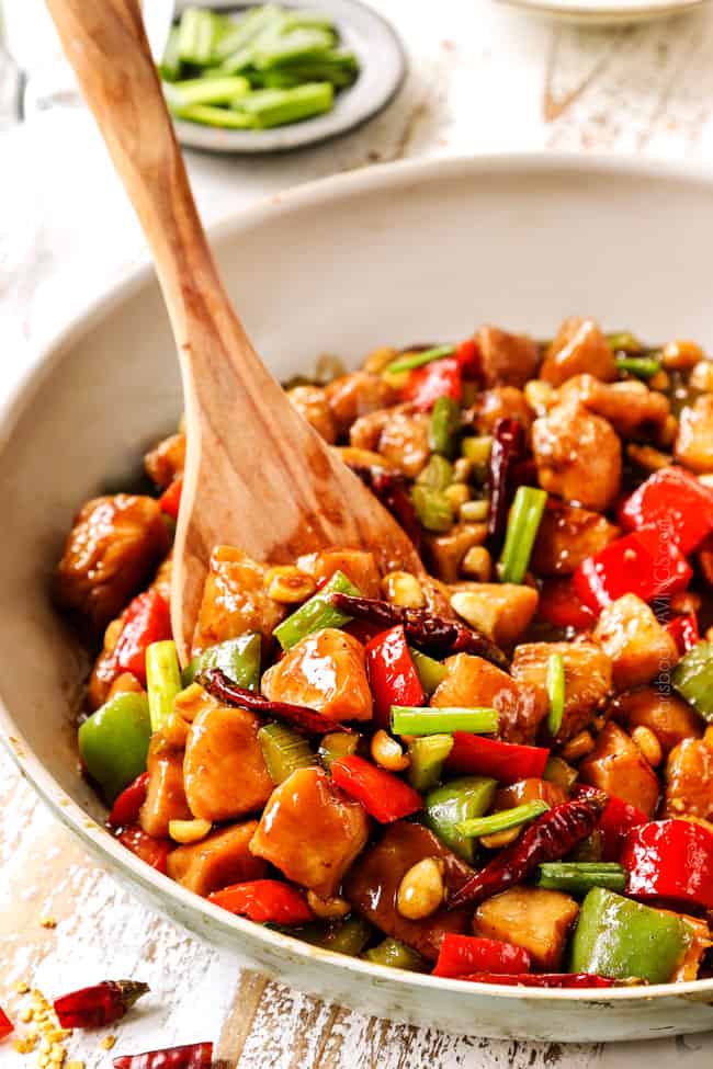 a wooden spatula serving best kung pao chicken form a white skillet