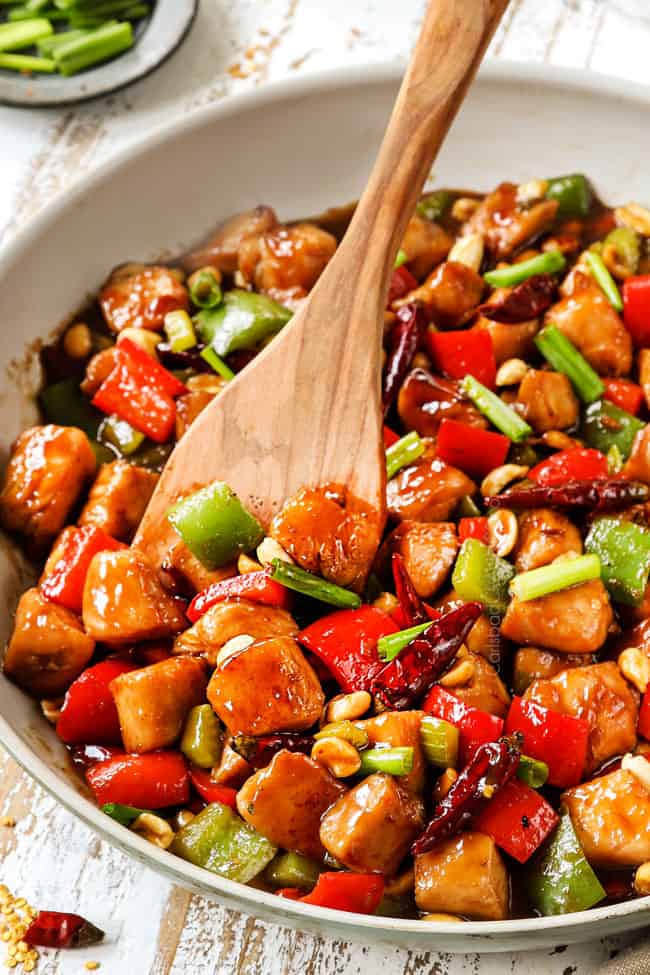 a wooden spatula serving best kung pao chicken form a white skillet
