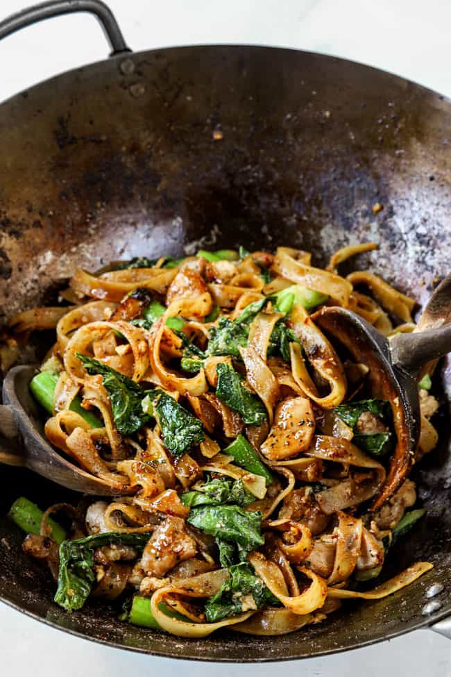 wooden tongs tossing pad see ew noodles together in a wok