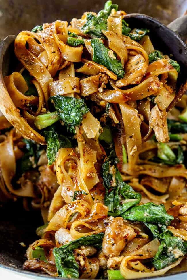 showing how to make pad see ew noodles by tossing chicken, Chinese broccoli and eggs and noodles together with wooden tongs.