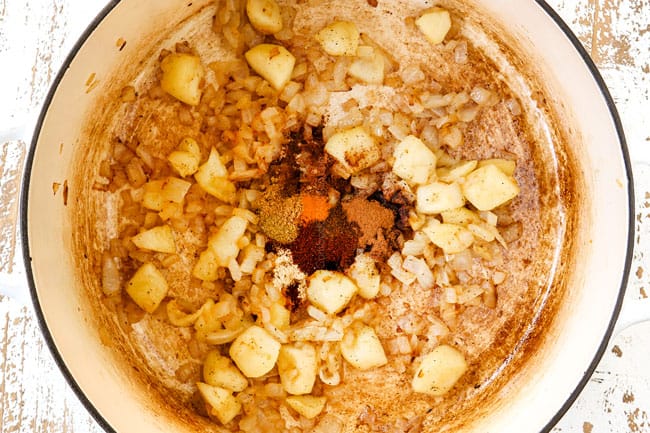 showing how to make pumpkin soup recipe by adding cinnamon, turmeric, ground coriander, ground nutmeg, ground cloves to the soup pot