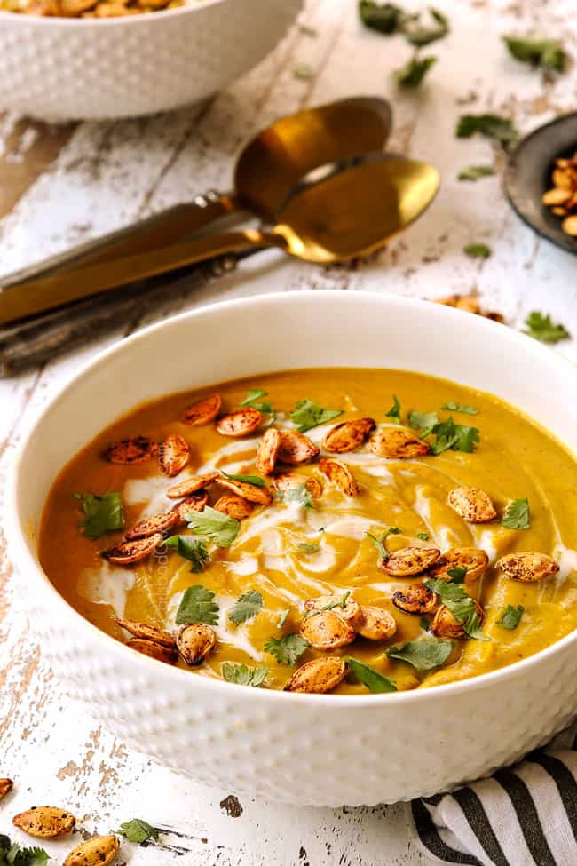 a white bowl of pumpkin coconut soup garnished with pumpkin seeds and cilantro