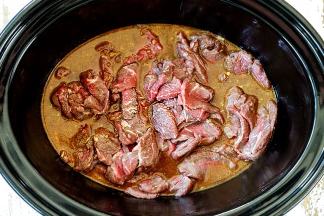 showing how to make slow cooker beef and broccoli recipe by adding thinly sliced steak to the crockpot
