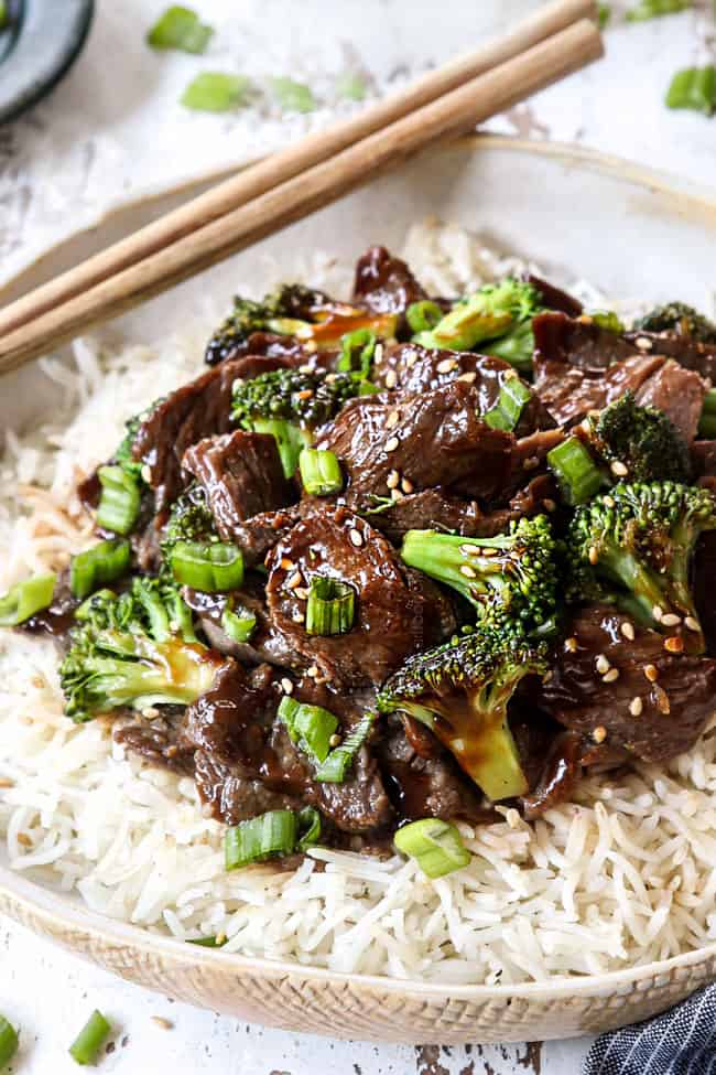 showing how to serve crockpot beef and broccoli recipe by adding to a bowl of white rice and garnishing with green onions and sesame seeds