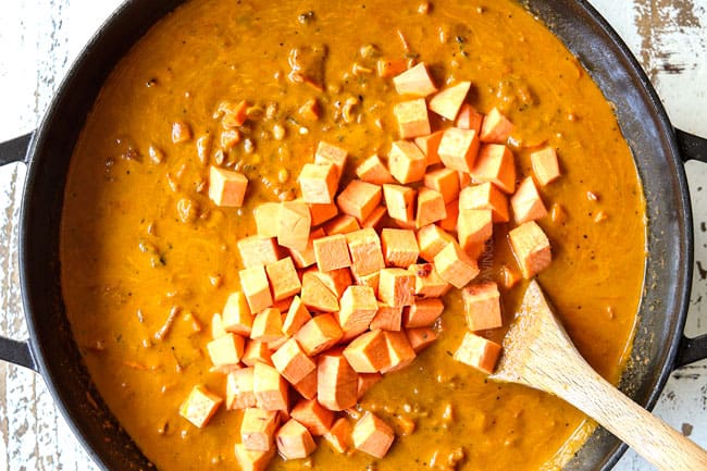 showing how to make lentil curry recipe by stirring in sweet potatoes in a black pot