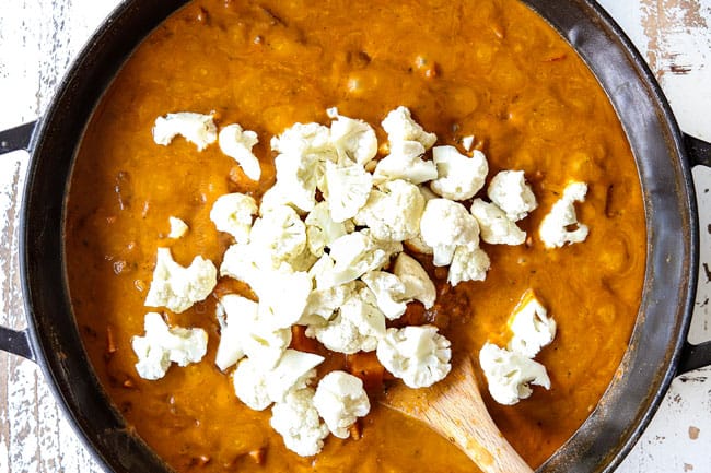 showing how to make lentil curry recipe by adding cauliflower to curry in a black pot