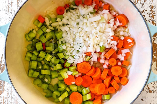 showing how to make leftover turkey rice soup by cooking carrots, onions and celery in a white Dutch oven