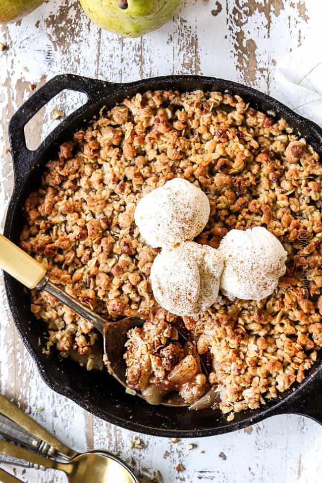 top view of pear crisp recipe in a cast iron skillet with three scoops of vanilla ice cream