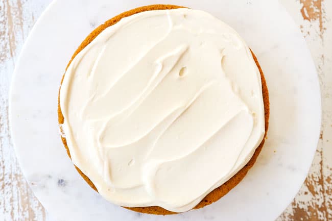 showing how to make pumpkin spice cake by spreading frosting on a cake
