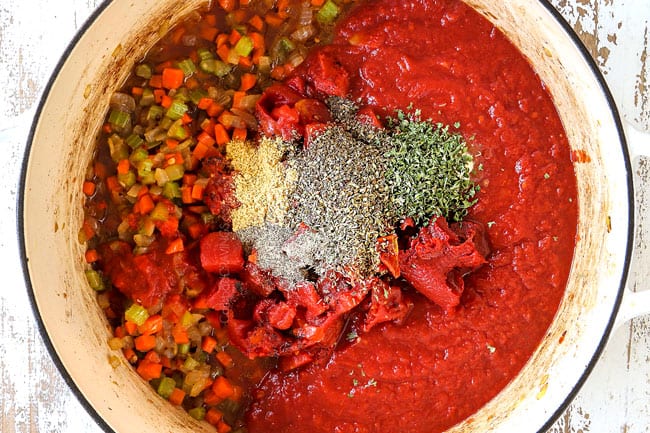 showing how to make Chicken Parmesan Pasta by adding crushed tomatoes, diced tomatoes and herbs to a large white pot