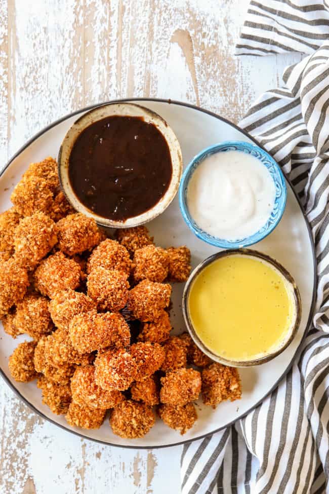 top view of homemade chicken nuggets on a white plate served with BBQ sauce, ranch and honey mustard dip