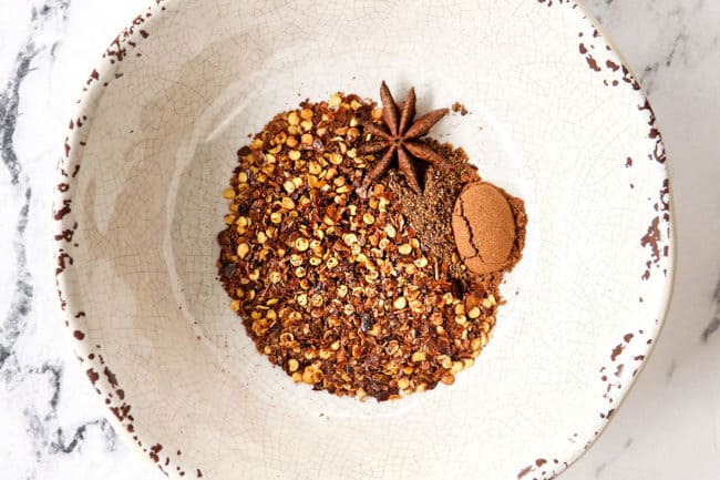 showing how to make Dan Dan Noodles recipe by adding red pepper flakes, Chinese 5 spice and szechuan powder to a bowl