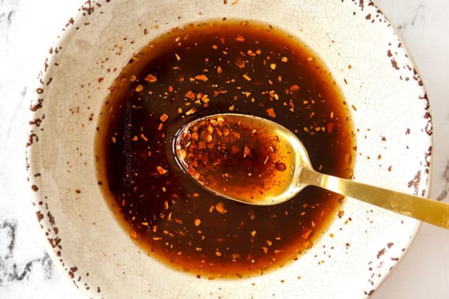 showing how to make Dan Dan Noodles recipe by adding red pepper flakes, chili oil and Chinese 5 spice too a bowl