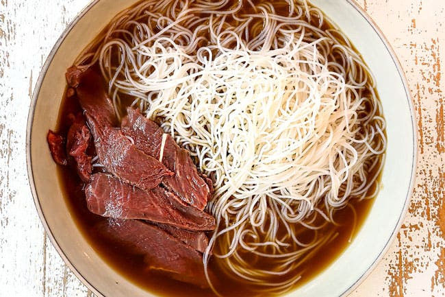 showing how to make pho by adding beef and noodles to a bowl with beef broth