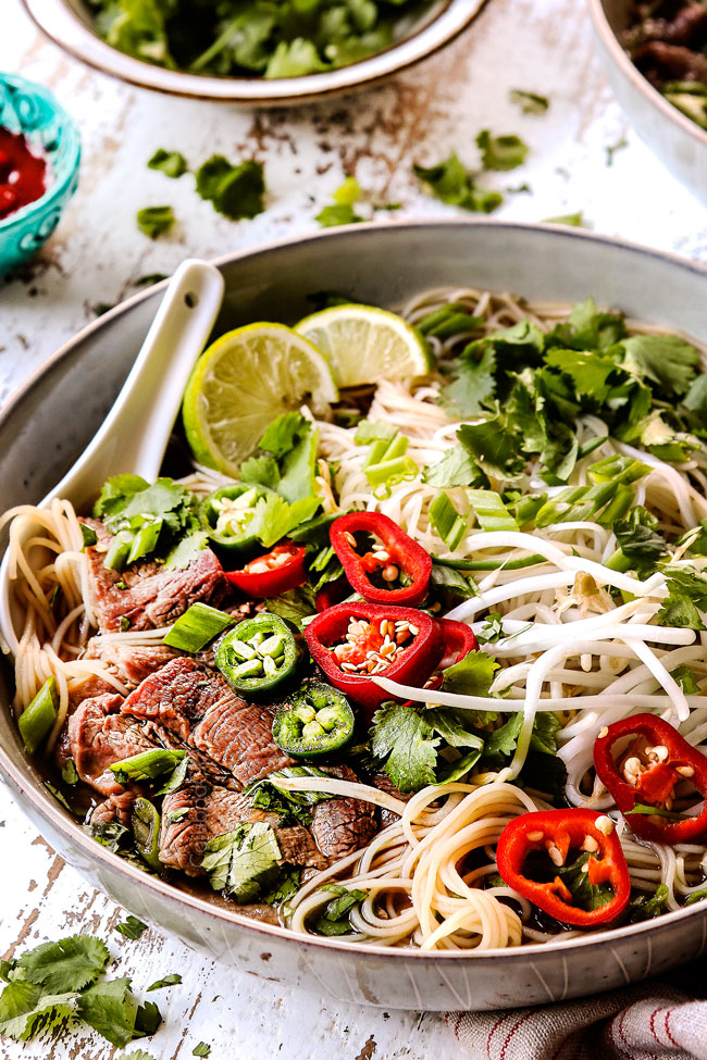 side view of a bowl of pho soup garnished with chili peppers, bean sprouts and cilantro