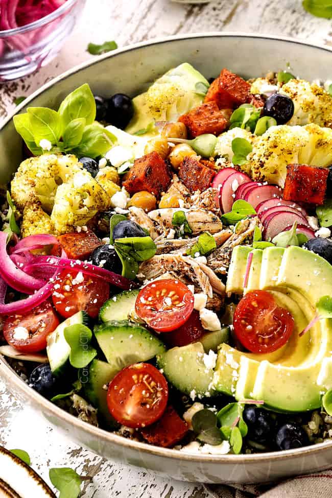 up close of a rice bowl recipe with chicken, tomatoes, pickled red onions, avocados and roasted vegetables