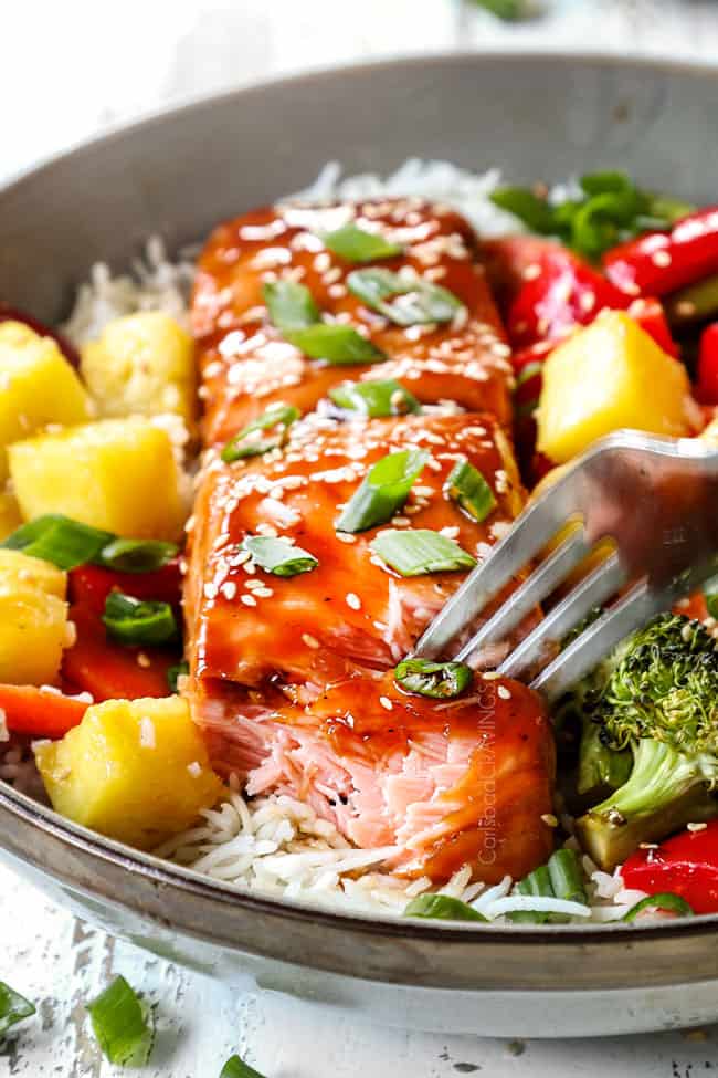 baked teriyaki salmon recipe in a bowl with a fork taking a bite showing how juicy the salmon is