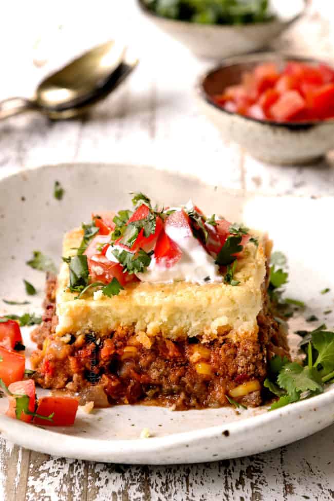 a slice of tamale pie on a plate topped with tomatoes, sour cream and cilantro