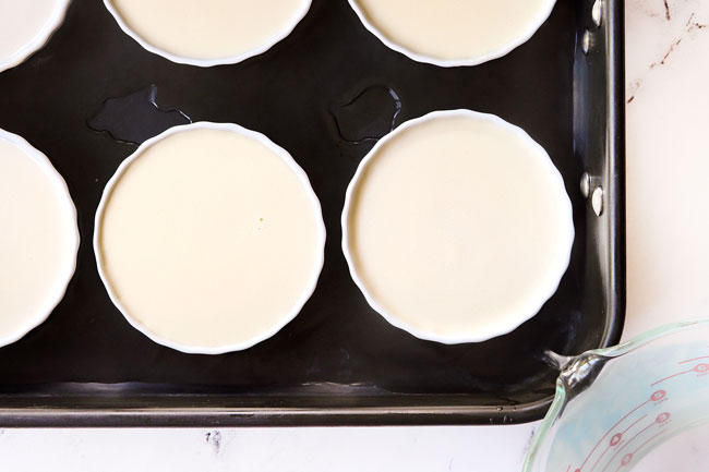 showing how to make creme brulee by pouring water around ramekins in a roasting pan to create a water bath