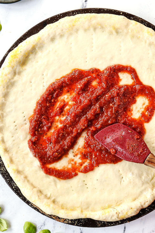 showing how to make margherita pizza by spooning margherita pizza sauce onto pizza dough