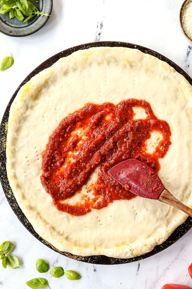 showing how to use pizza sauce recipe by spreading it onto pizza dough with a spatula