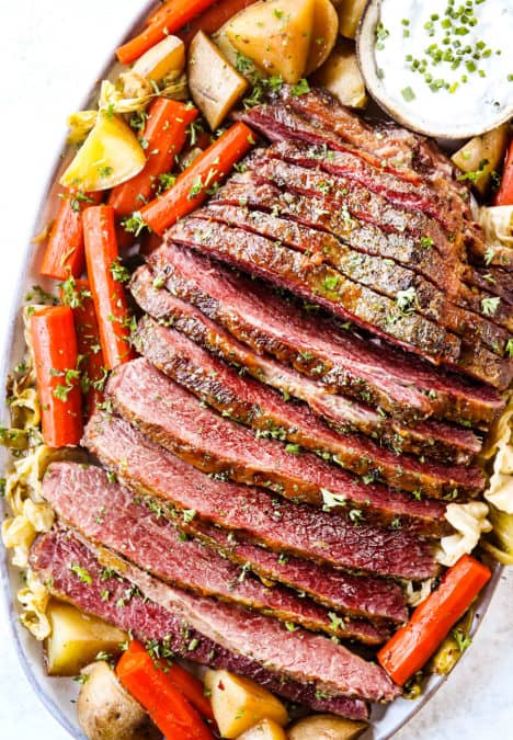 top view of corned beef and cabbage on a platter with potatoes, carrots and horseradish sauce