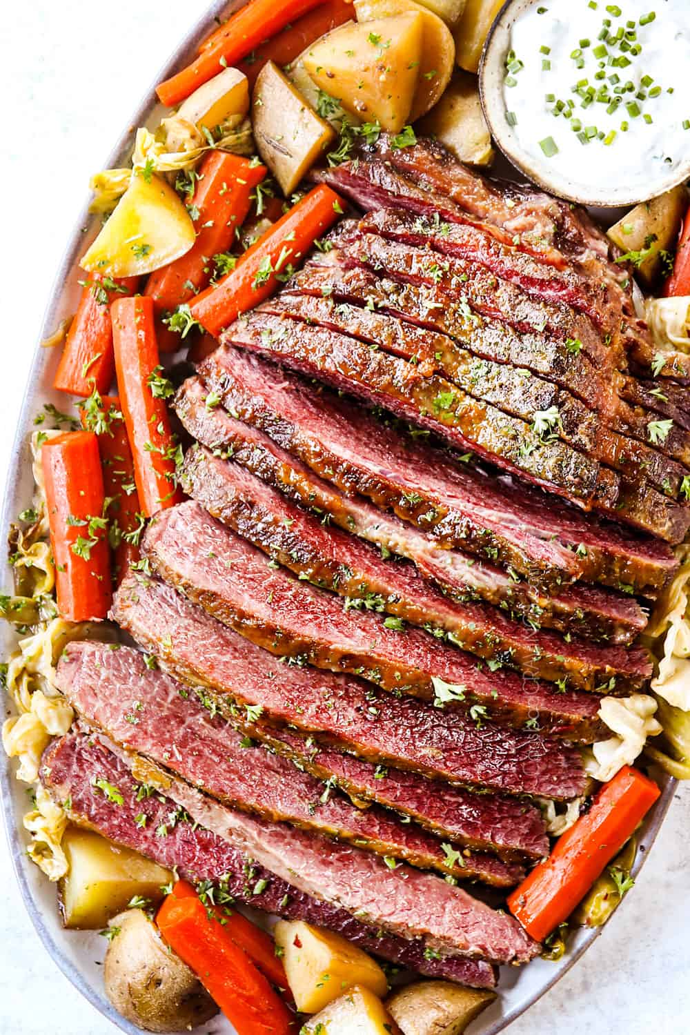 top view of corned beef and cabbage on a platter with potatoes, carrots and horseradish sauce